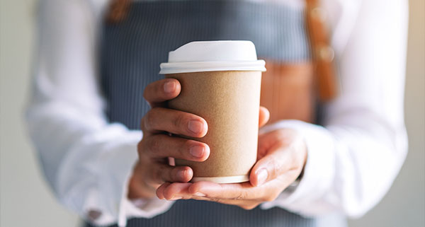 a barista holding a takeaway cup of coffee to the camera