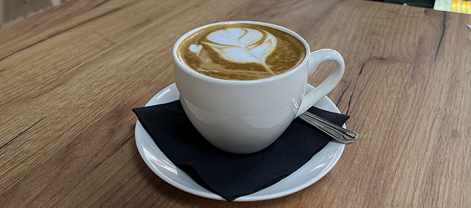 a cup of coffee with latte art on top, on a wooden countertop in Patisserie Luxe, a patisserie in Poole