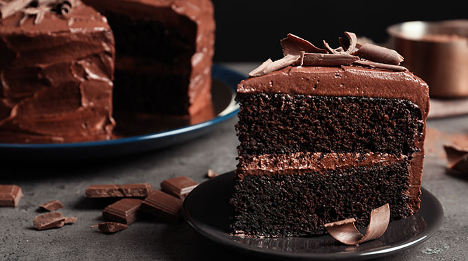 a slice chocolate cake on a plate with a chocolate cake in the background