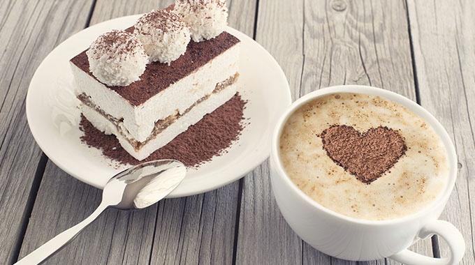 a cup of coffee with a latte art heart on top next to a plate with a slice of tiramisu on it